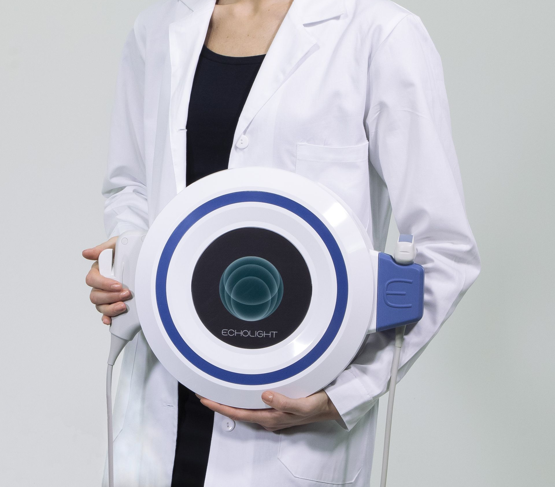 Person in a white lab coat holding a round white-and-blue medical device against a light background