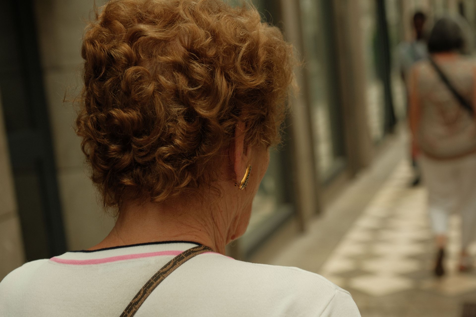 Back view of a person with curly hair walking down a hallway with checkered floor tiles