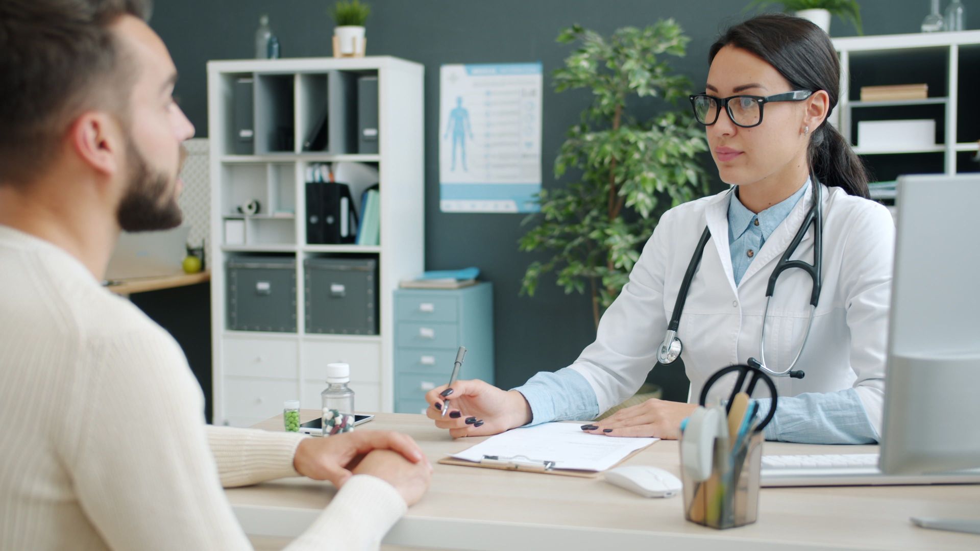 Doctor speaking with a patient in a bright clinic office at a desk.