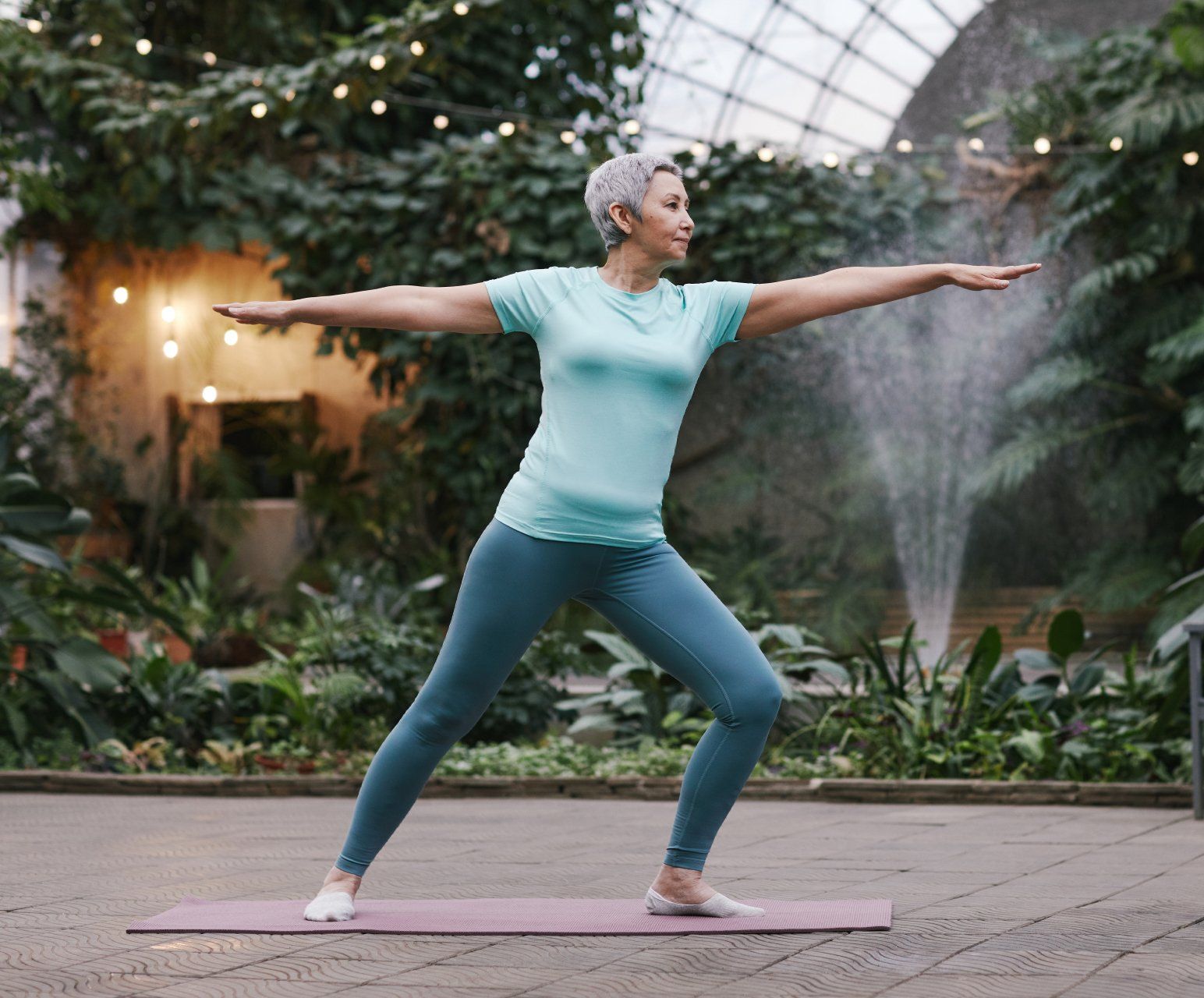 A woman is standing on a yoga mat with her arms outstretched.