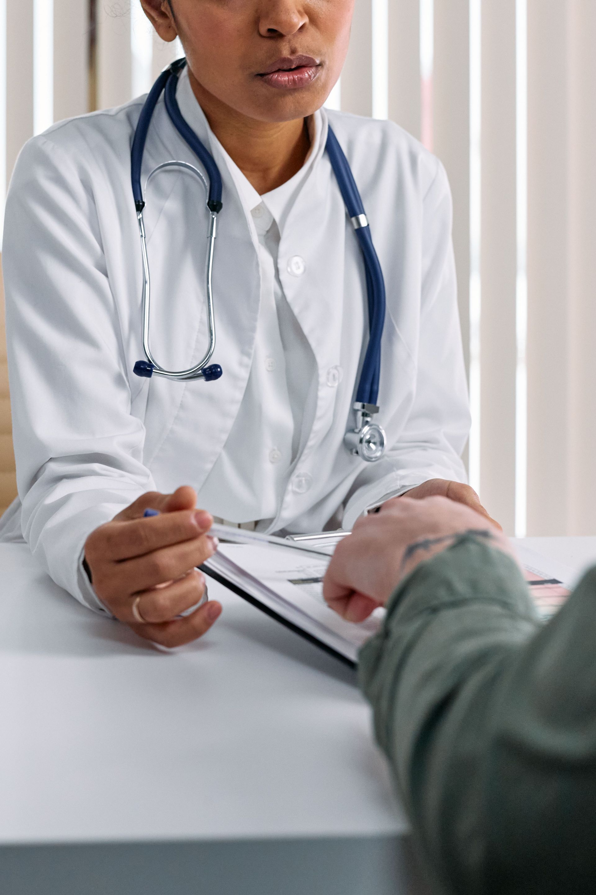 Doctor in white coat with stethoscope consulting a patient at a desk