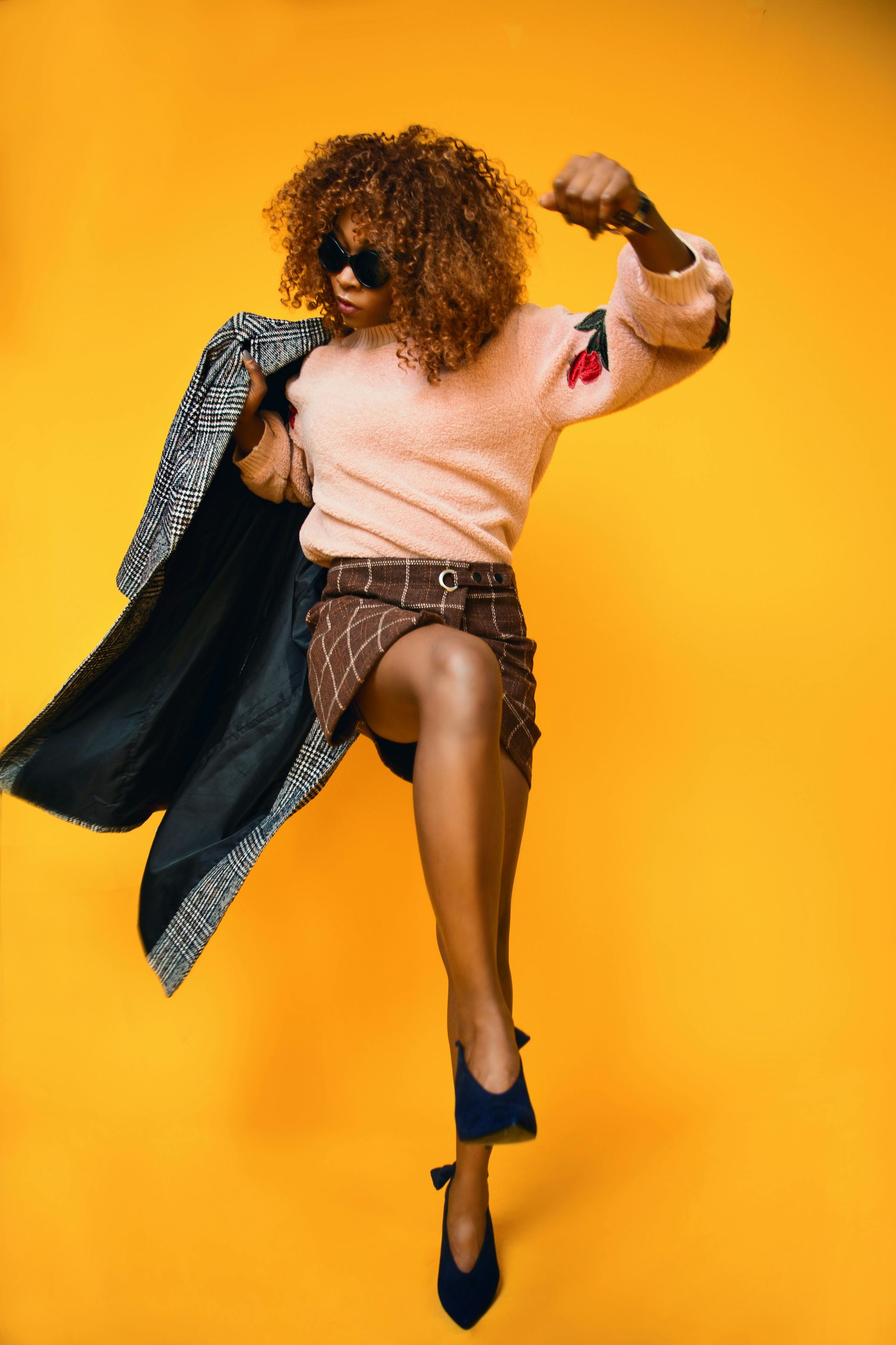 Person jumping in a pink sweater and patterned coat against a bright yellow background