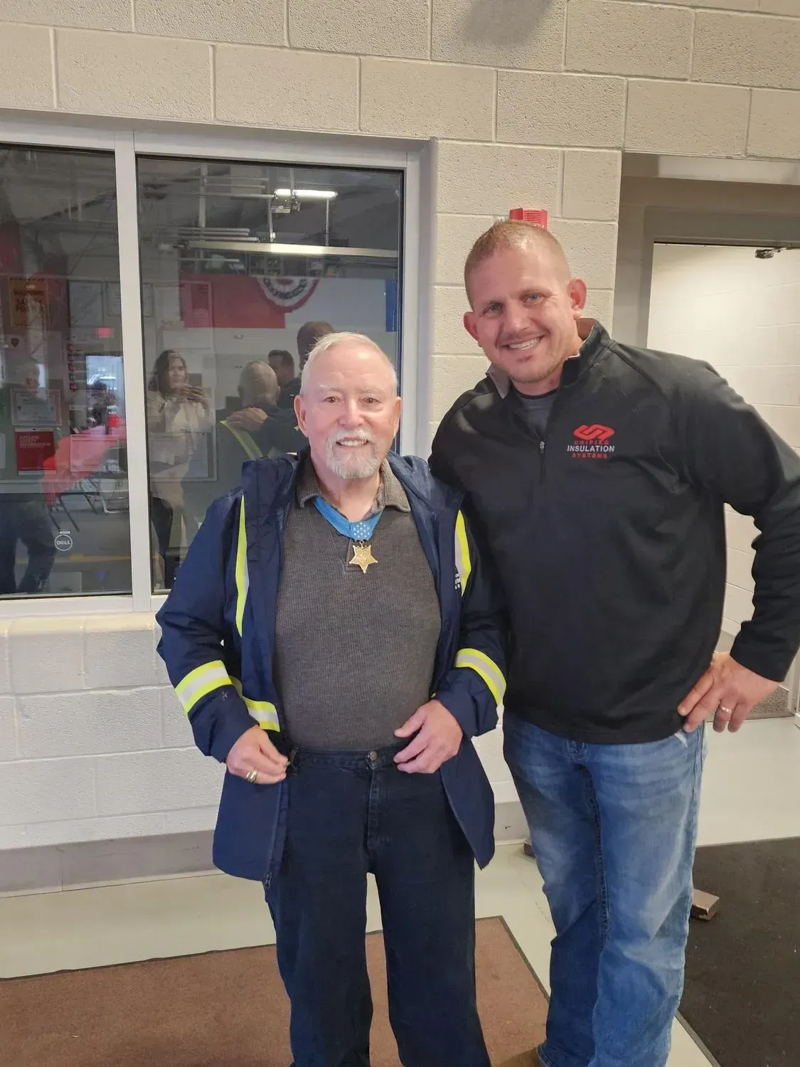 Two men standing outside a storefront, smiling for a photo.