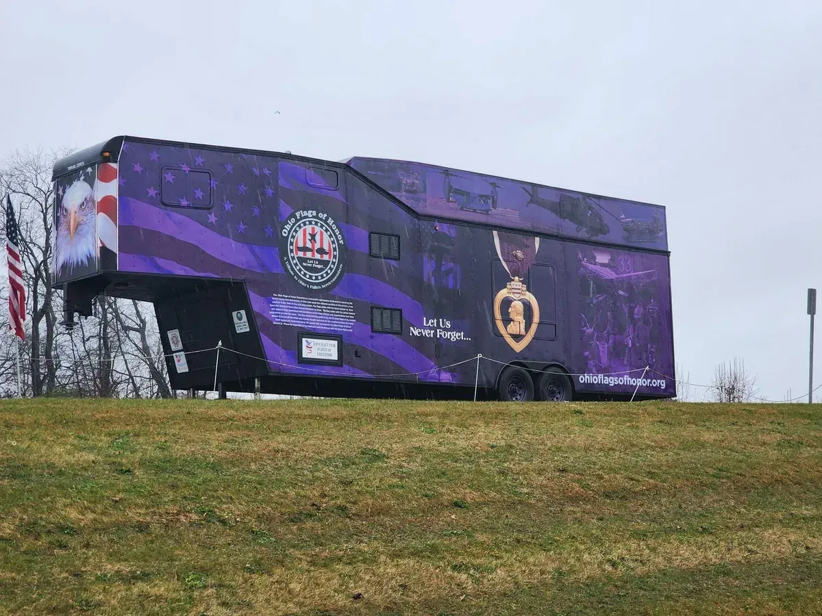 Purple mural-covered trailer on a grassy hill under an overcast sky