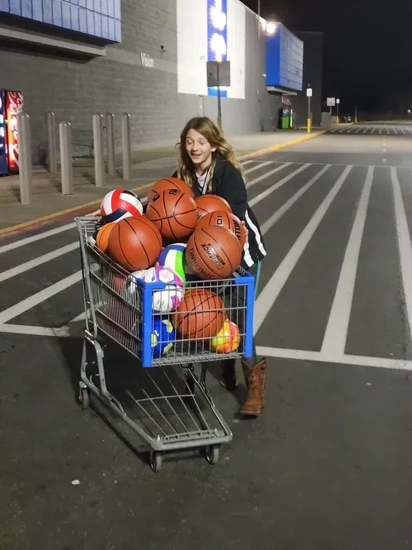 Person standing by a shopping cart full of basketballs outside a store at night
