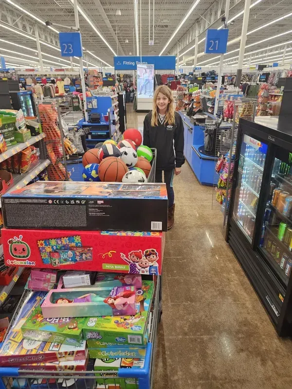 Woman in a toy aisle holding a ball, with colorful toys and shelves in a store.