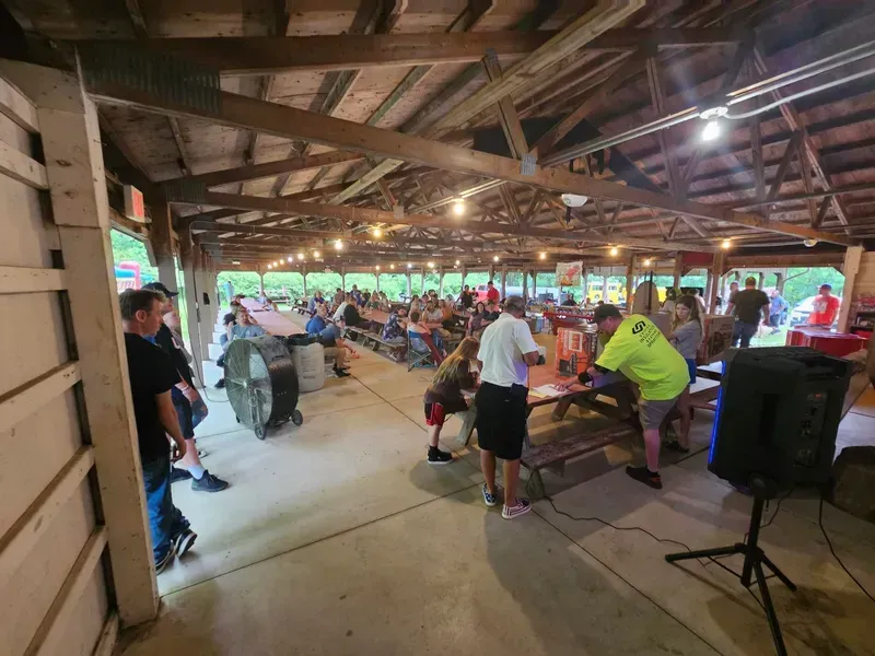 Crowded open-air pavilion with people seated at long tables under wooden beams and lights