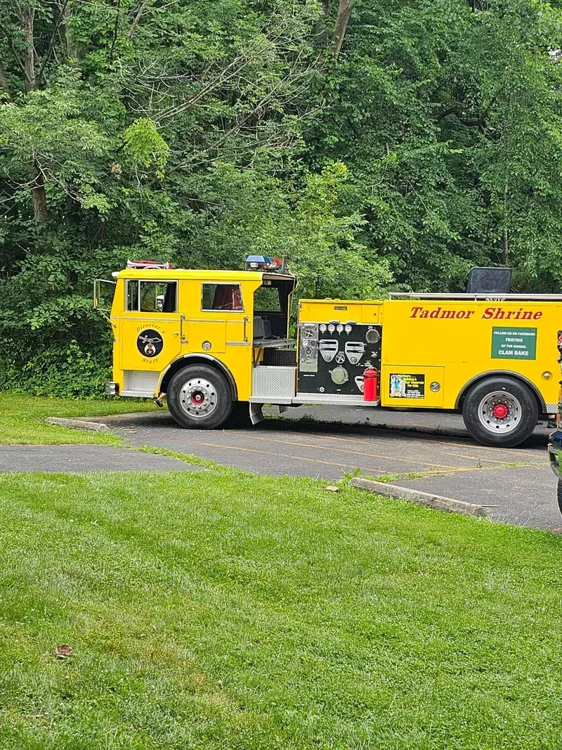 Yellow vintage truck parked on a gravel drive beside green trees and grass.
