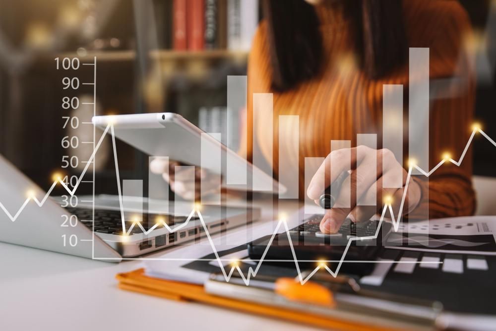 A Woman is Sitting at a Desk Using a Laptop and a Cell Phone — Gem Socials In Laurieton, NSW