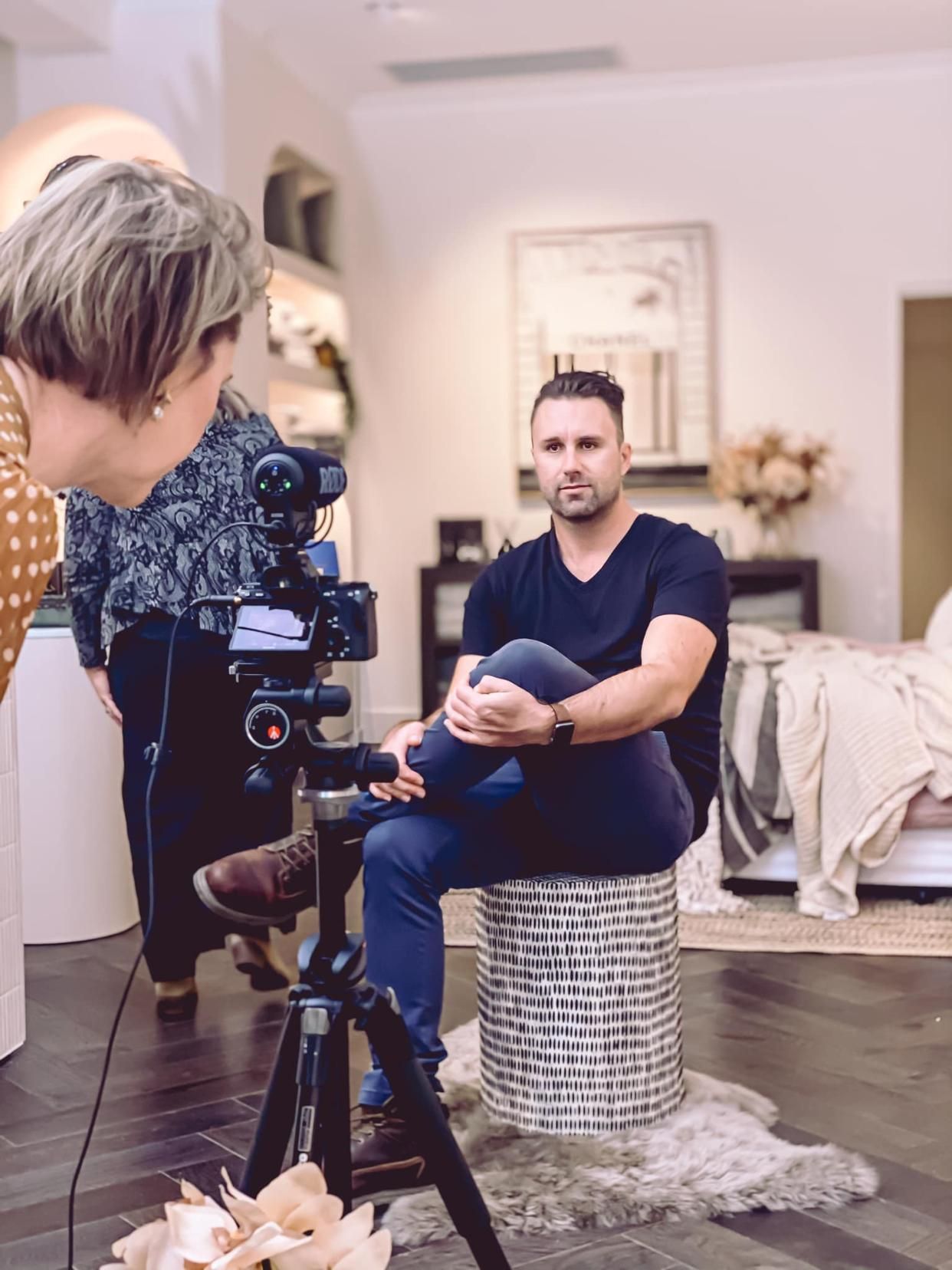A Woman is Taking a Picture of a Man Sitting on a Stool in Front of a Camera — Gem Socials In Port Macquarie, NSW