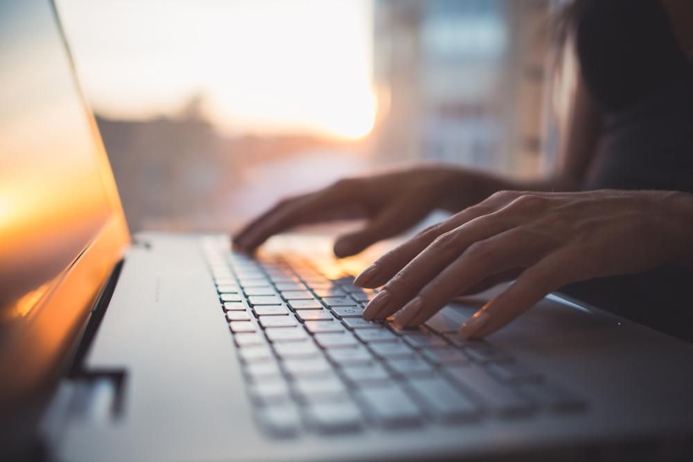 A person is typing on a laptop computer at sunset. — Gem Socials In Port Macquarie, NSW