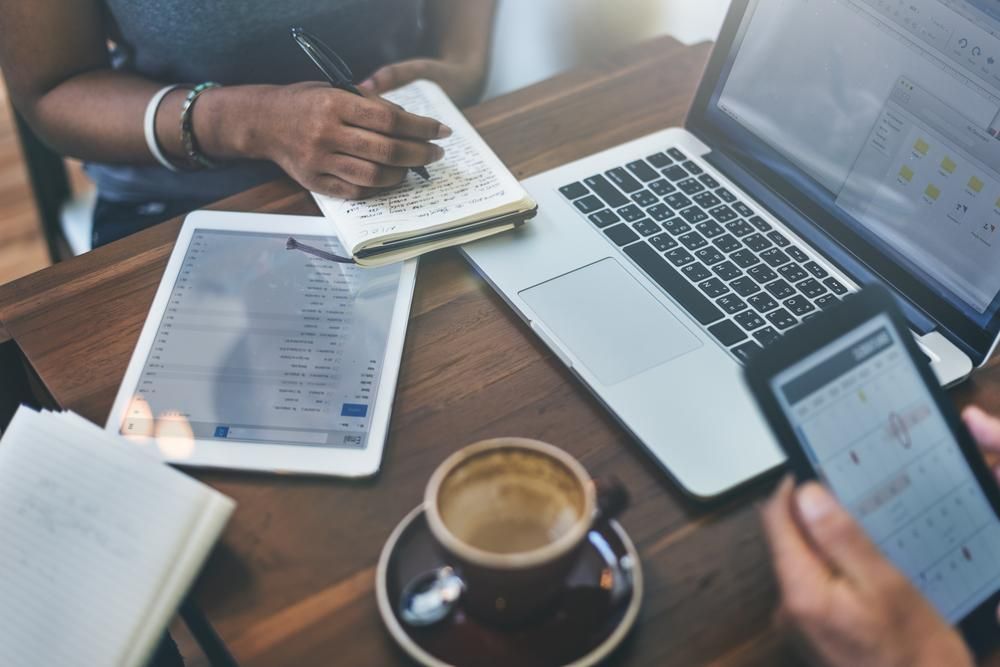 A Woman is Sitting at a Table With a Laptop, Tablet, and Cell Phone — Gem Socials In Port Macquarie, NSW