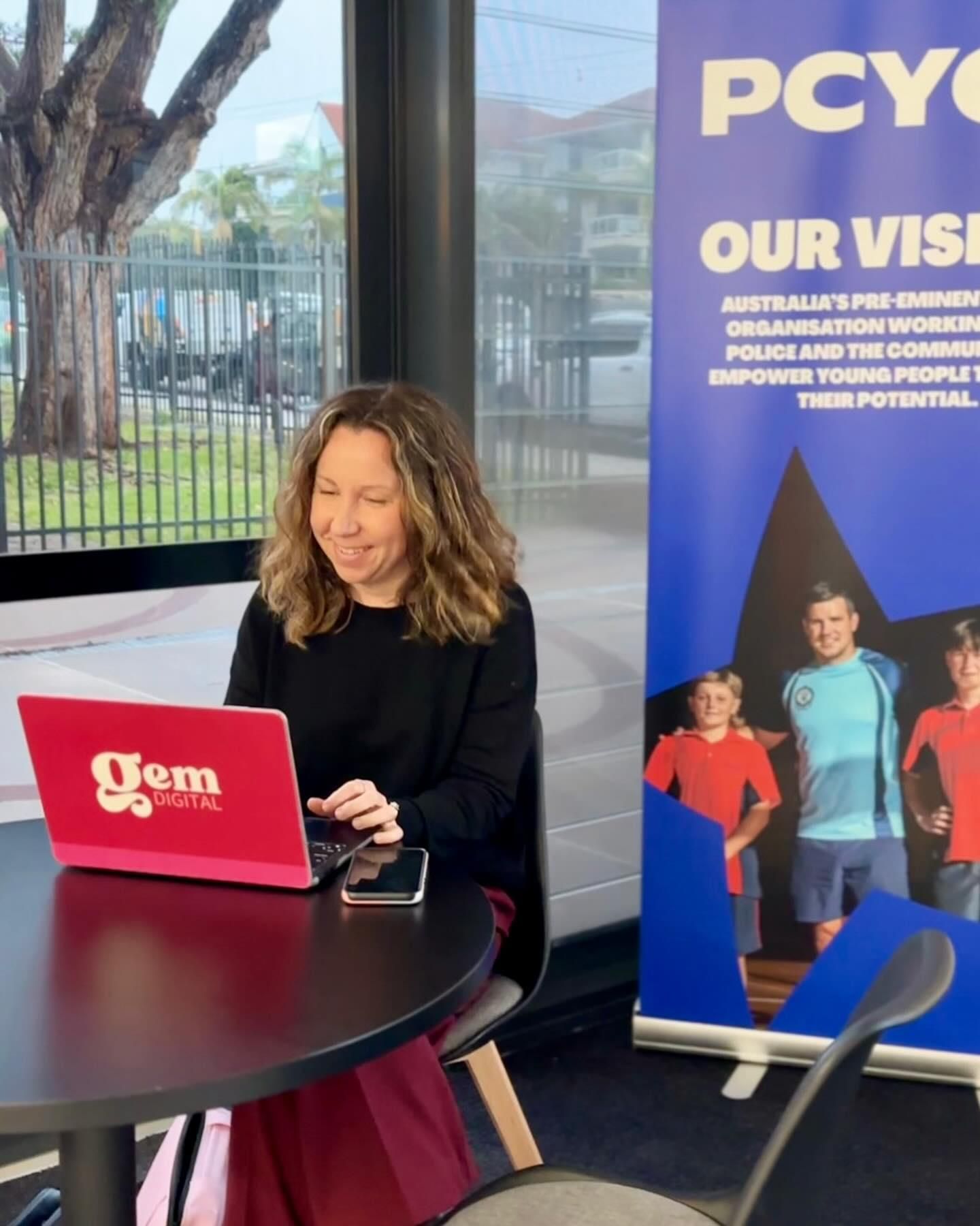A Woman is Sitting at a Table Using a Red Gem Laptop — Gem Socials In Coffs Harbour, NSW