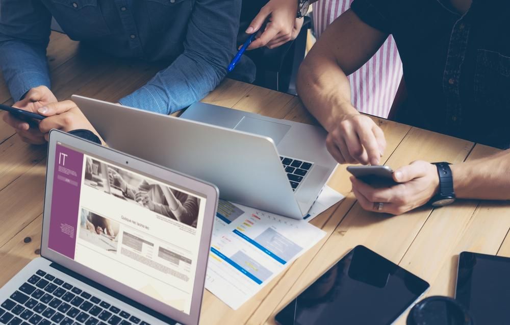 A Group of People Are Sitting at a Table With Laptops and a Cell Phone — Gem Socials In Lake Cathie, NSW