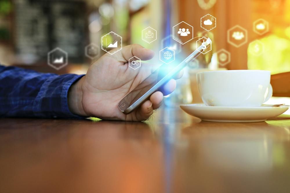 A Person is Using a Smart Phone While Sitting at a Table With a Cup of Coffee — Gem Socials In South West Rocks, NSW