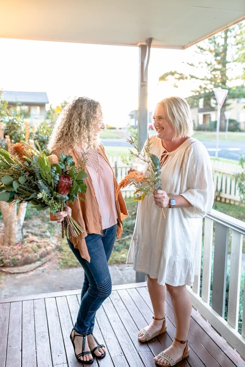 Two women are standing on a porch holding flowers — Gem Socials In Port Macquarie, NSW
