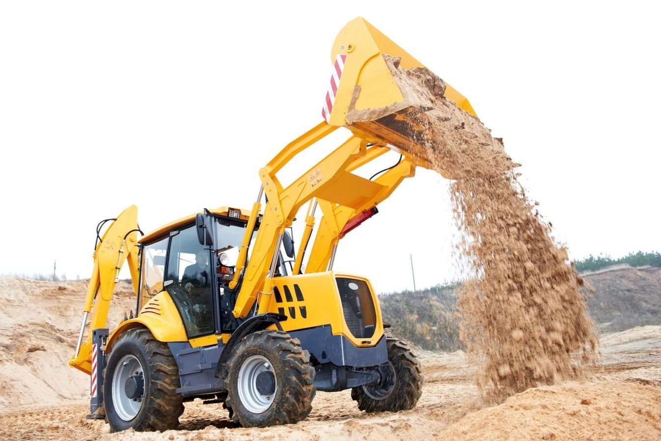 a medium size backhoe with its bucket in the air actively dumping dirt.  Palmdale, Ca