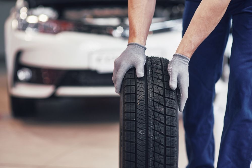 A Man Is Holding A Tire In Front Of A Car — East Lismore Automotive in  East Lismore, NSW