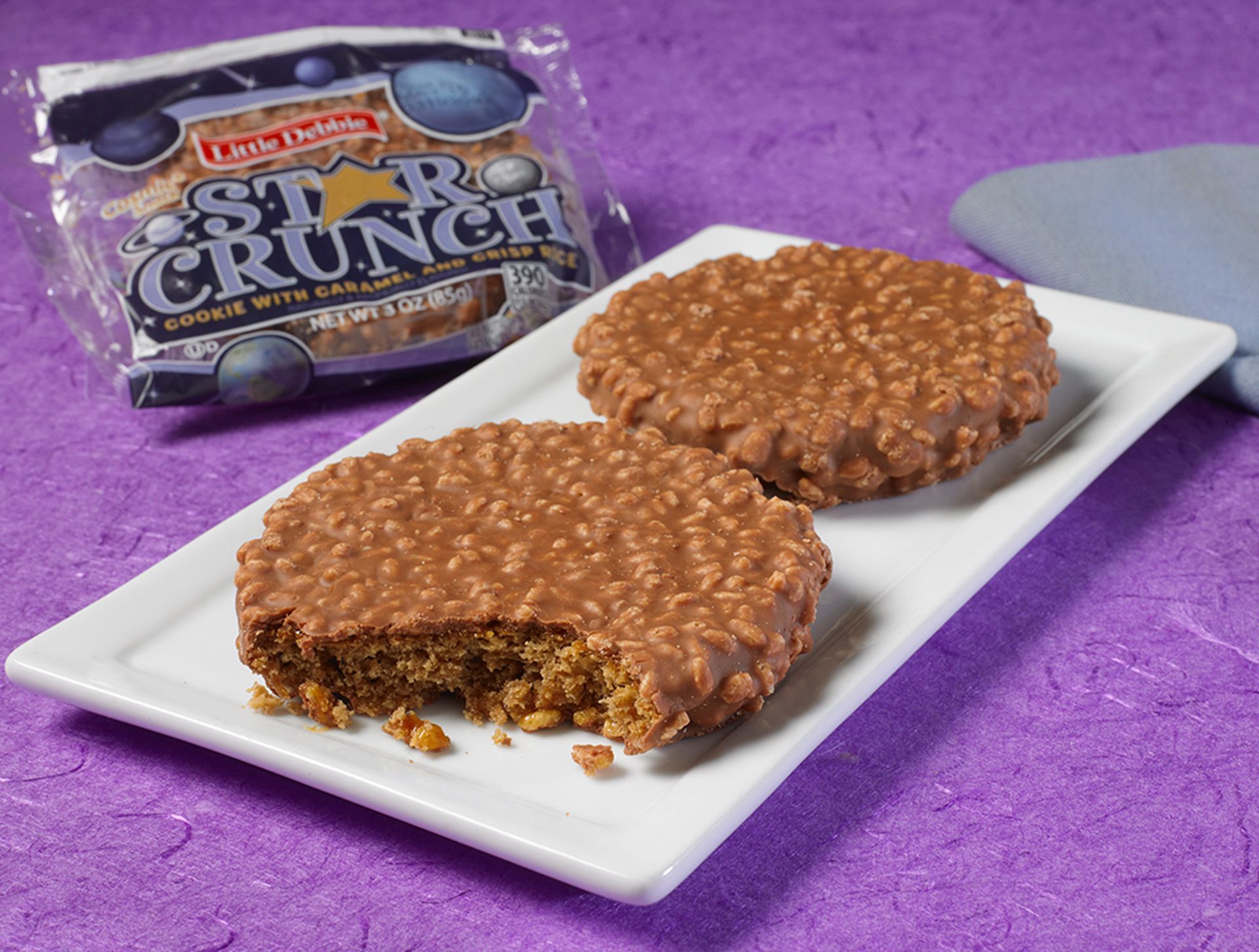 two single serve star crunch cookies on a white plate next to a wrapped one