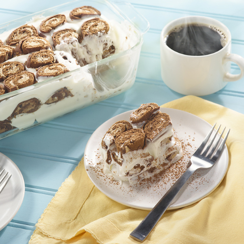 mocha swiss roll tiramisu in a glass dish and a slice on a white plate with a fork and yellow napkin