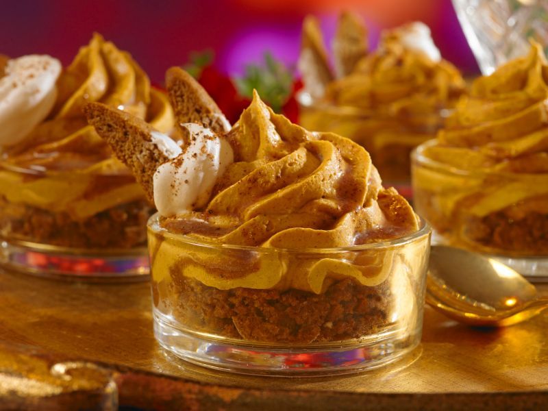 A close up of a dessert in a glass with a spoon on a table.
