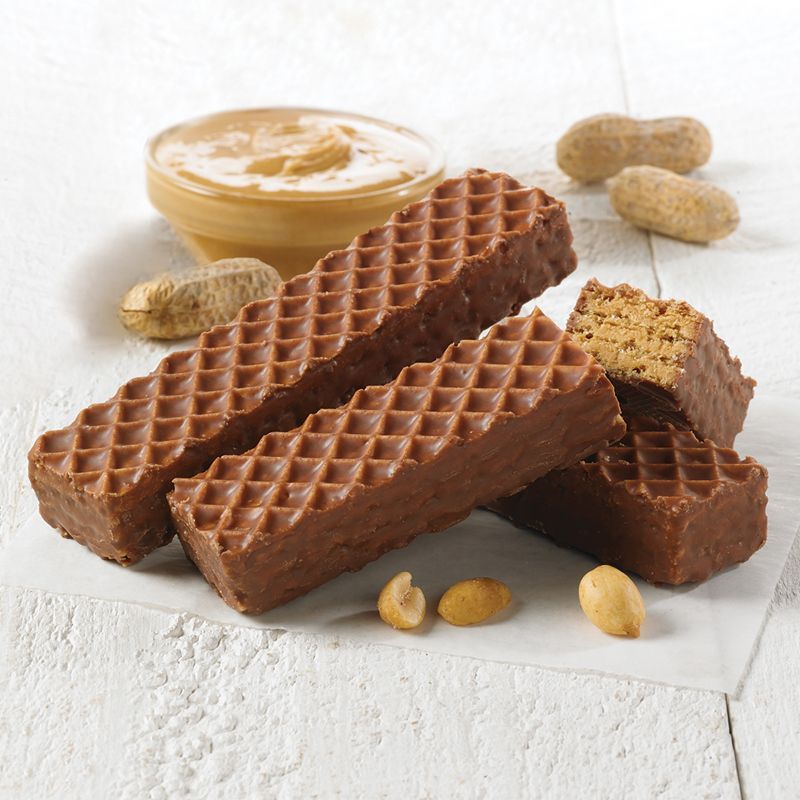 three nutty buddy wafer bars sitting on a wooden board with peanut butter and peanuts around 