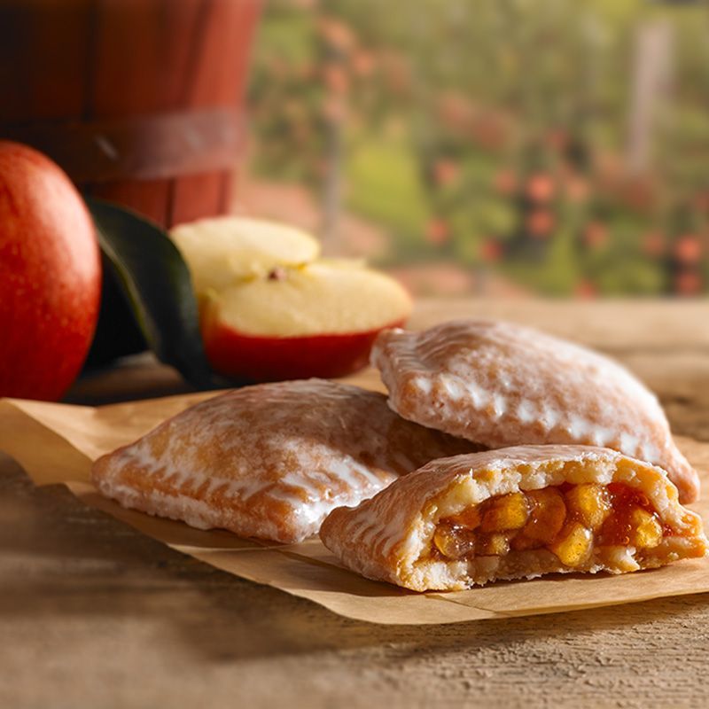 three apple pies with one broken in half sitting on a wooden board with red apples in the background