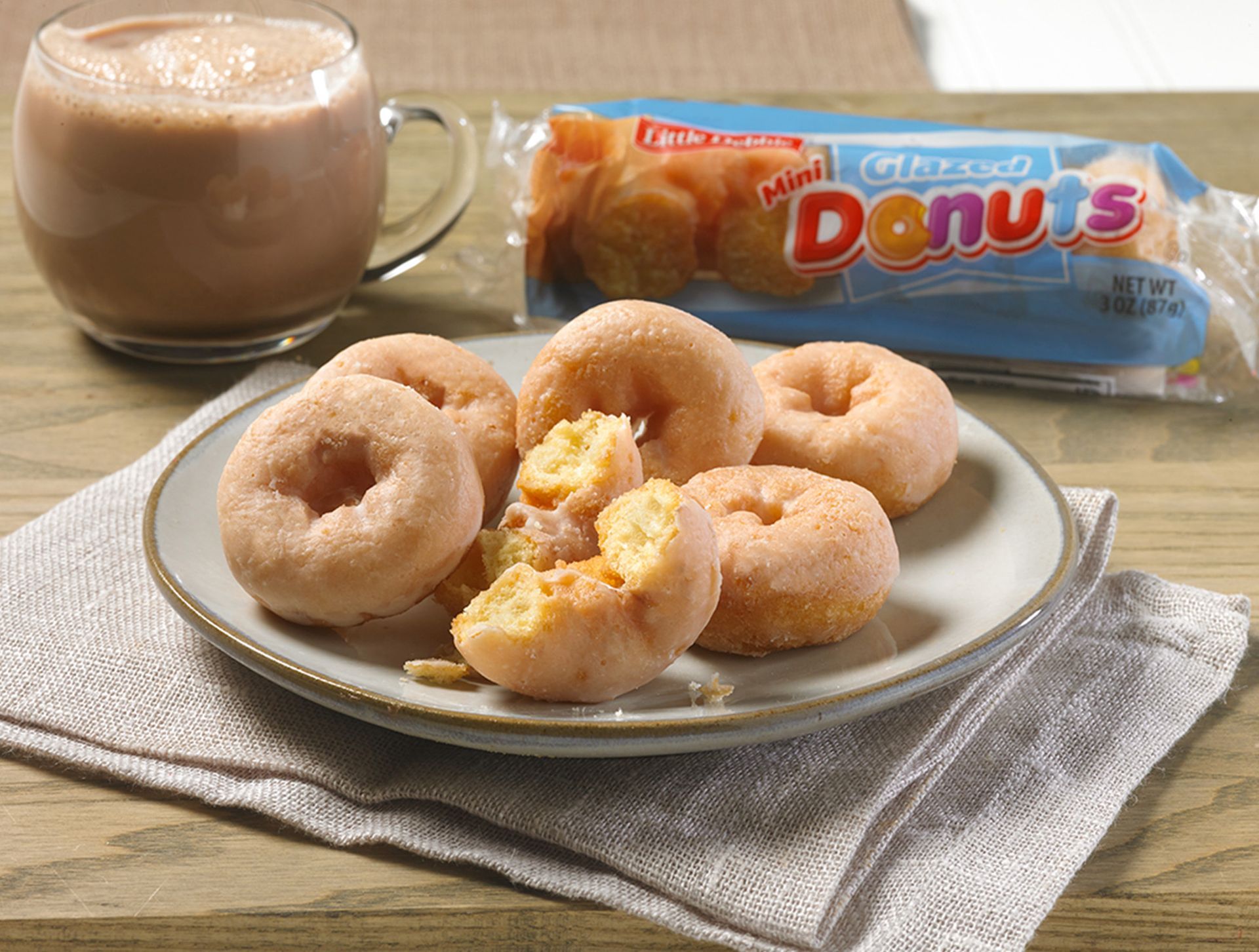 group of glazed mini donuts on a plate next to a cup of coffee and a package