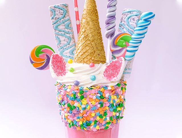 A milkshake decorated to look like a unicorn with ice cream cones , lollipops , and sprinkles.