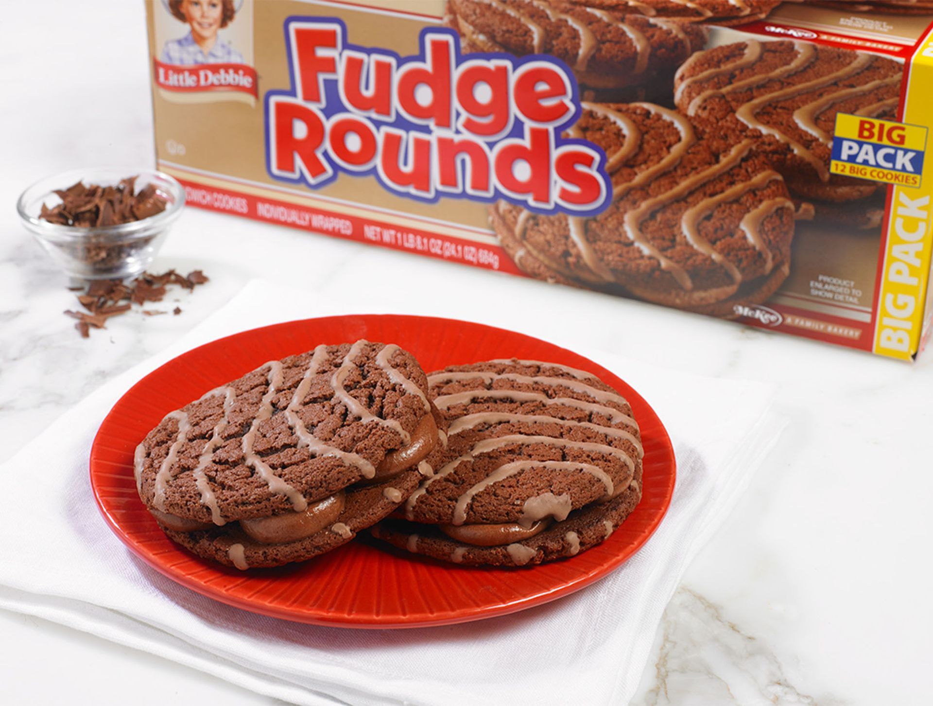two fudge rounds on a red plate next to a carton of big pack fudge rounds