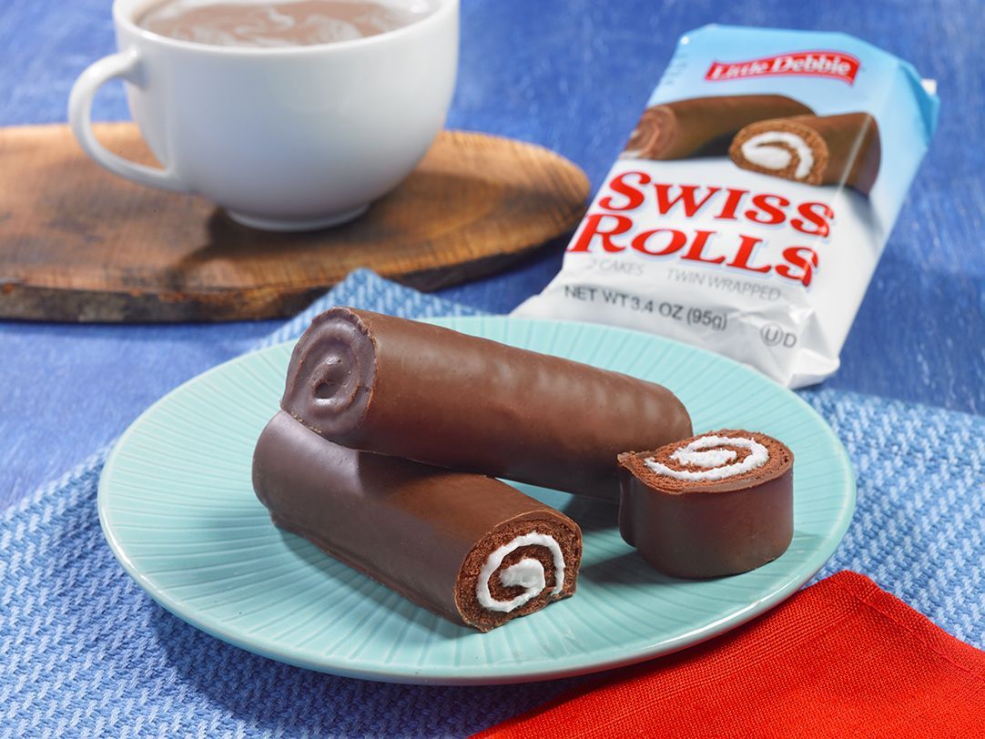Two swiss rolls on a blue plate next to a bag of swiss rolls