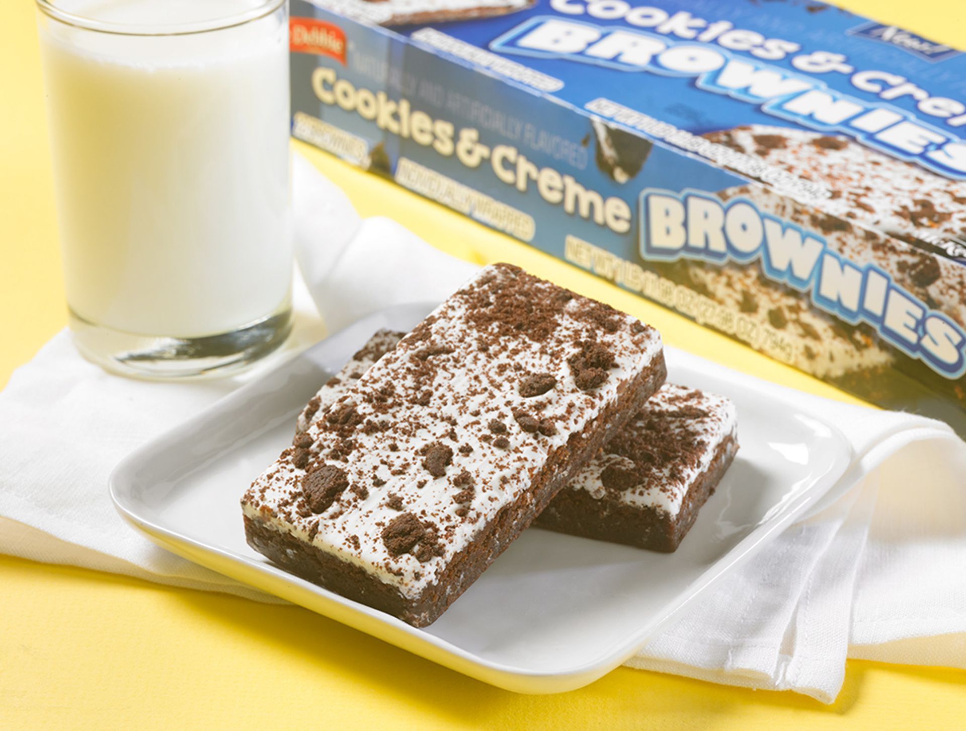 two cookies and creme brownies with a box in the background next to a glass of milk