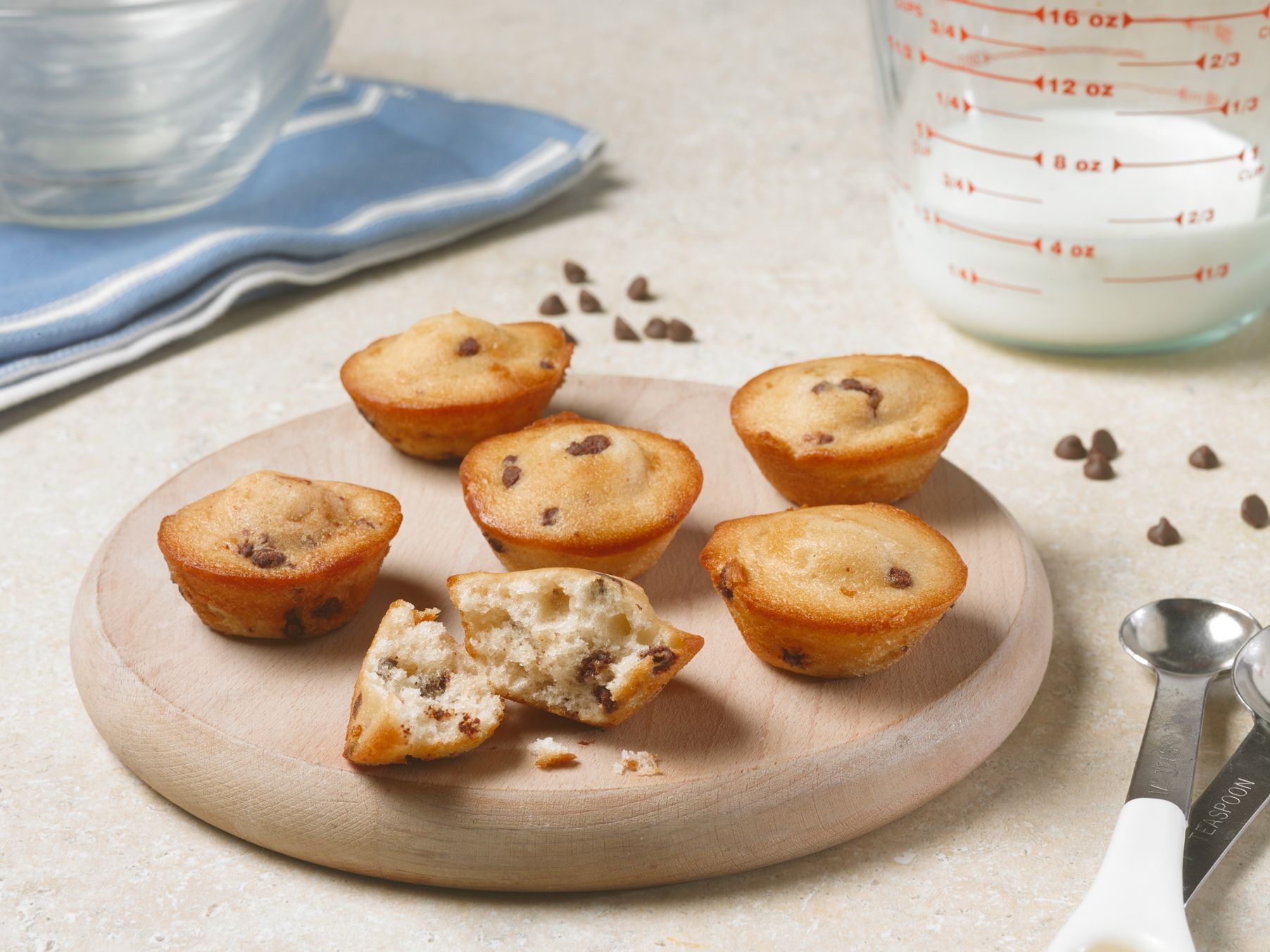 A wooden cutting board with muffins and a measuring cup of milk