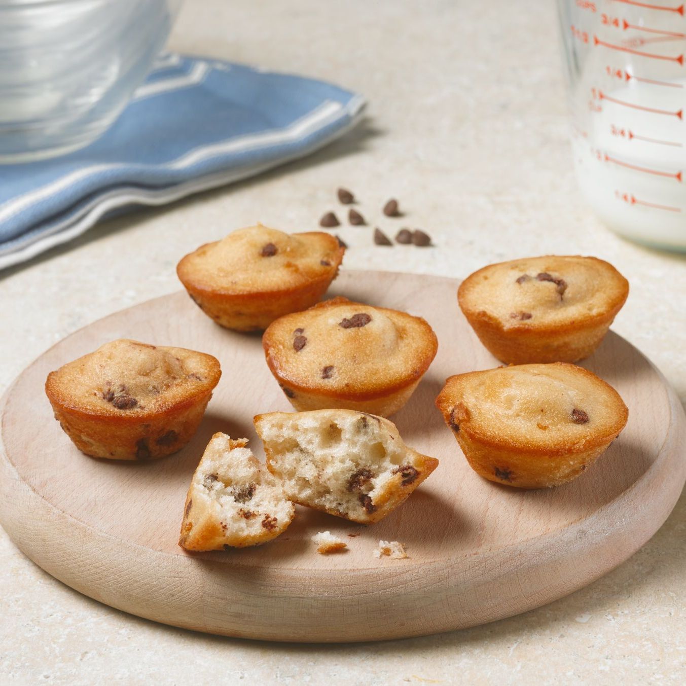 A wooden cutting board with muffins on it with one missing a bite