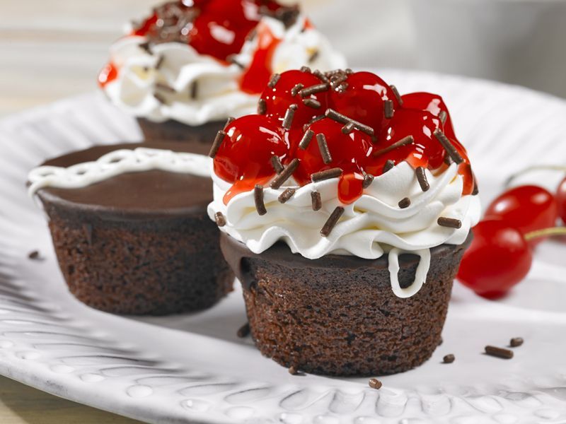 Three chocolate cupcakes with whipped cream and cherries on top