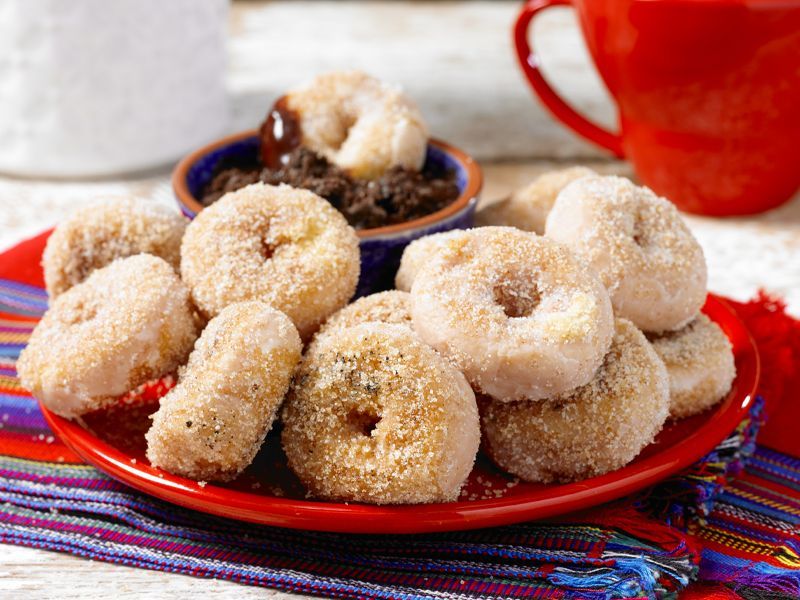 A red plate topped with churro style donuts and a cup of coffee.