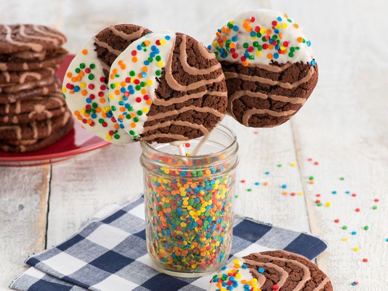 A jar filled with chocolate cookies and sprinkles on sticks.