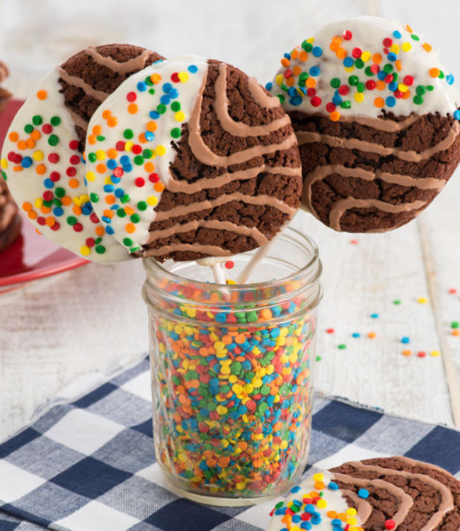 A jar filled with chocolate cookies and sprinkles on sticks.