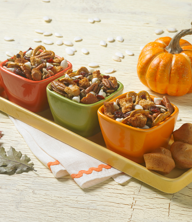 mini muffins mixed with nuts, pretzels and candy corn in three colored bowls with a pumpkin