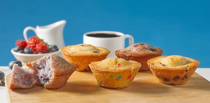 a group of mini muffins sitting on a wooden board with a blue background and a cup of coffee with fruit