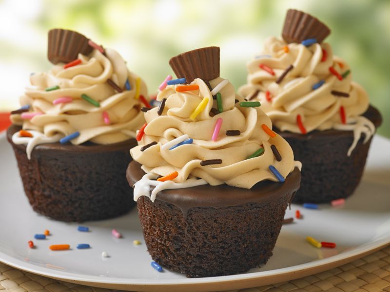 Three chocolate cupcakes with peanut butter frosting and sprinkles on a white plate