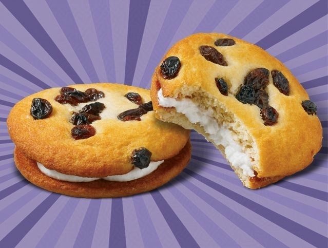 Two cookies with raisins and whipped cream on a purple background