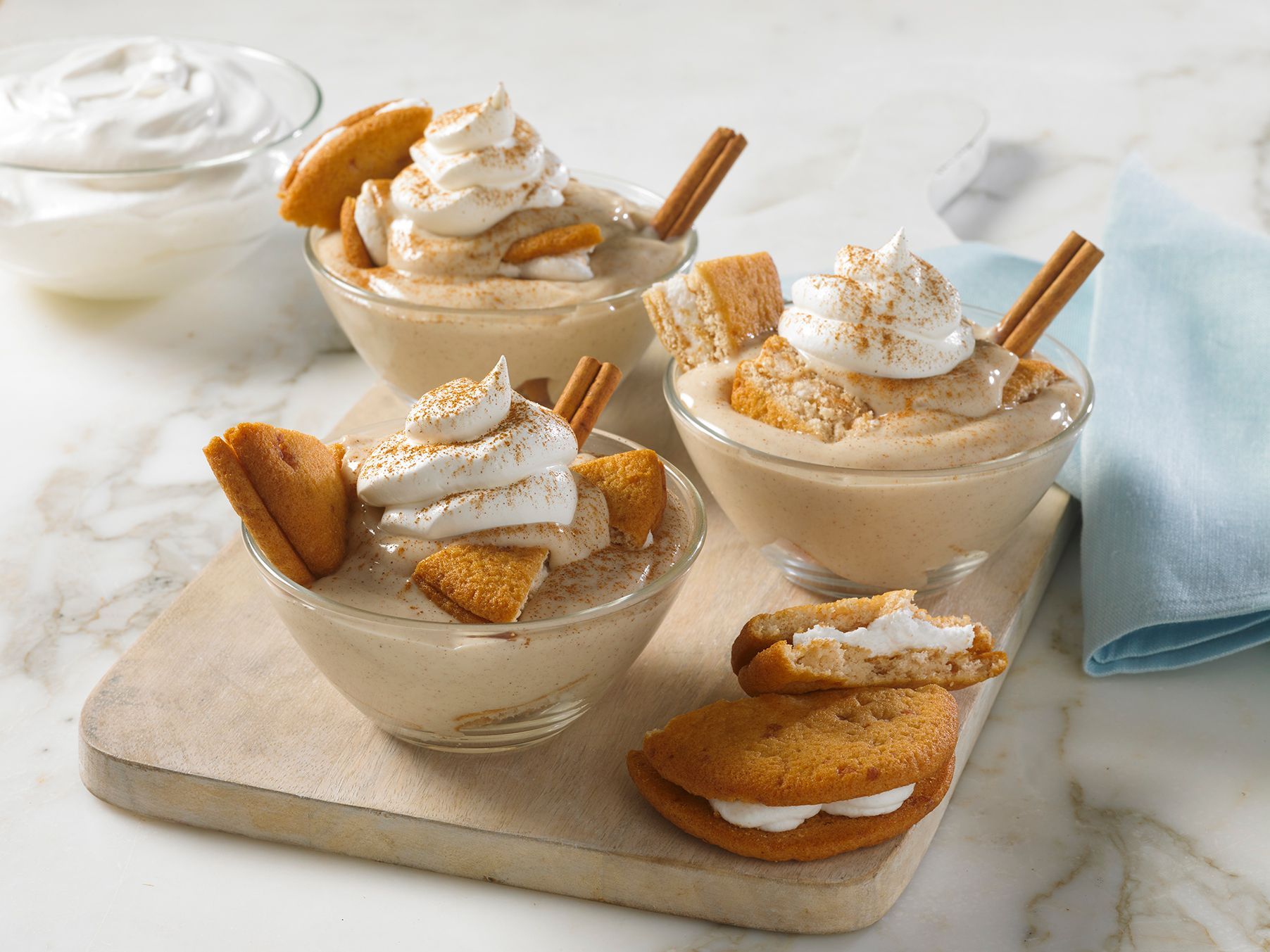 Three bowls of dessert with cookies and whipped cream on a cutting board.