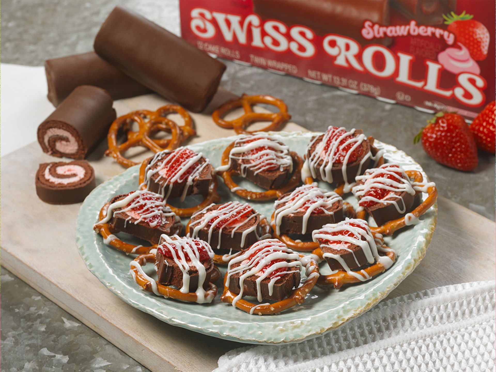 A plate of swiss rolls with pretzels and strawberries