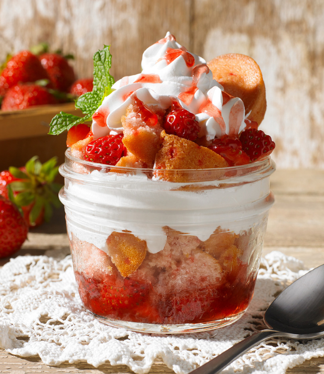 A strawberry shortcake dessert in a mason jar with whipped cream and strawberries.