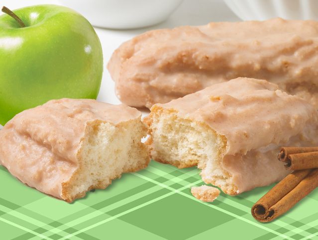 A donut with a bite taken out of it next to an apple and cinnamon sticks
