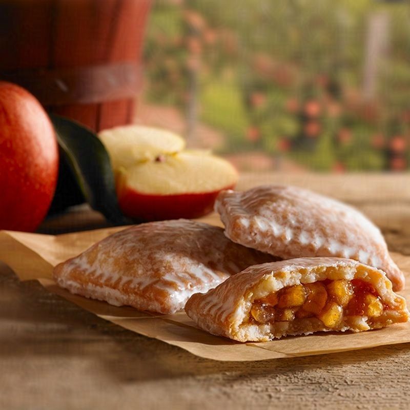 three apple pies with one broken in half sitting on a wooden board with red apples in the background