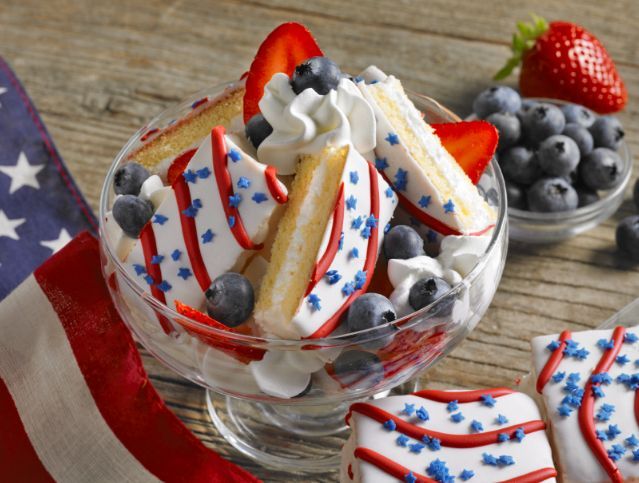 A dessert with strawberries , blueberries and whipped cream in a glass bowl.