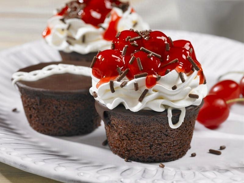 Three chocolate cupcakes with whipped cream and cherries on top