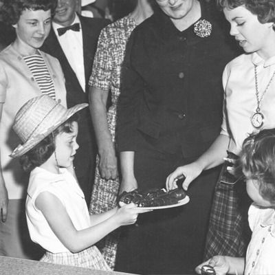 A little girl is holding a plate of food in front of a group of people